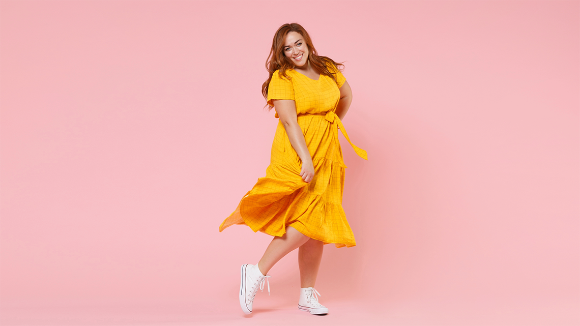 Happy woman of an apple body shape in a yellow dress on a pink background